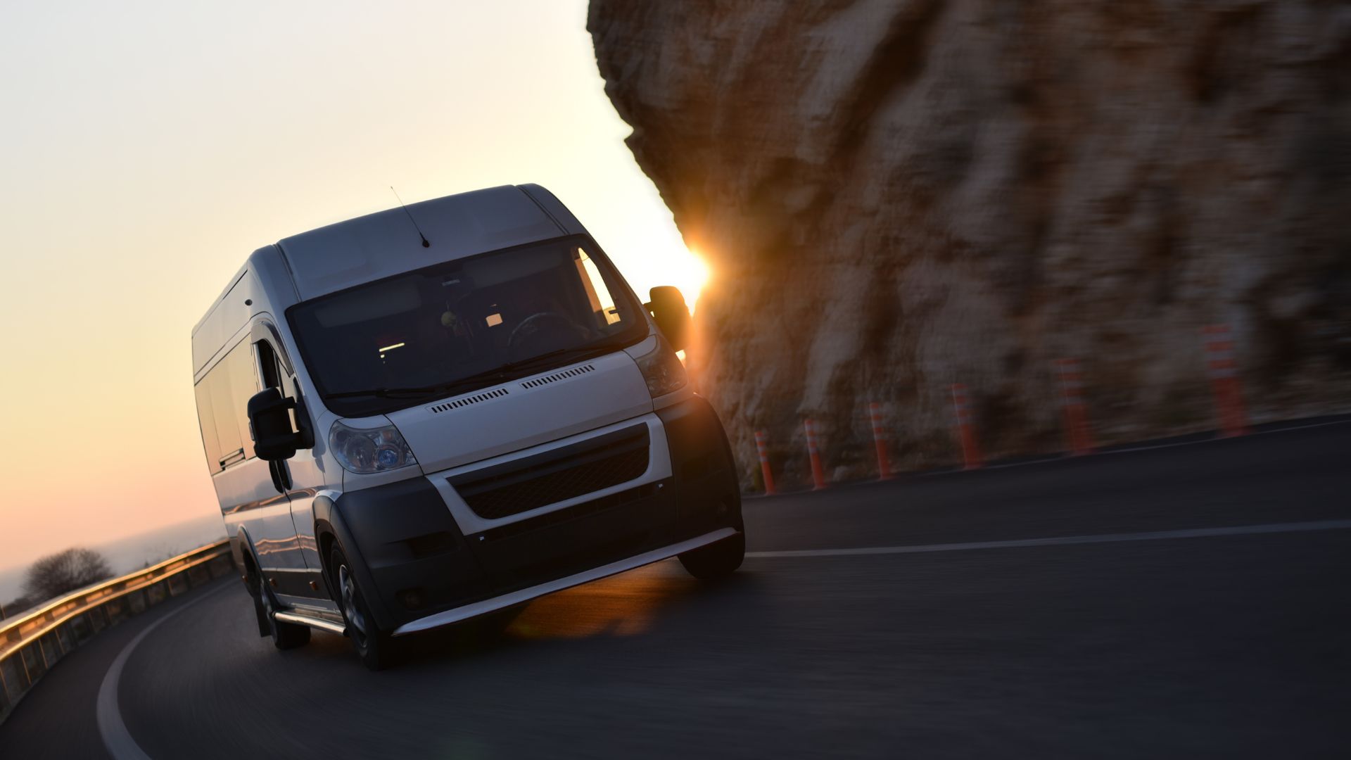A white van driving down a road next to a cliff