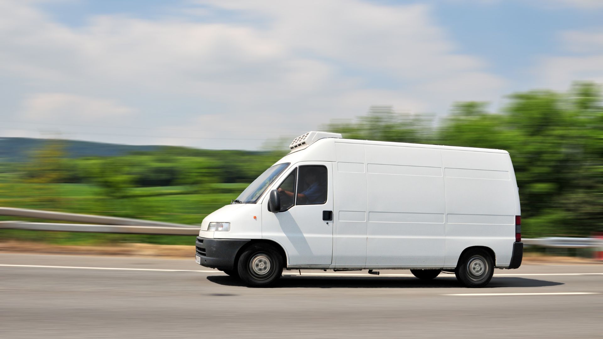 A white van driving down a road next to a forest